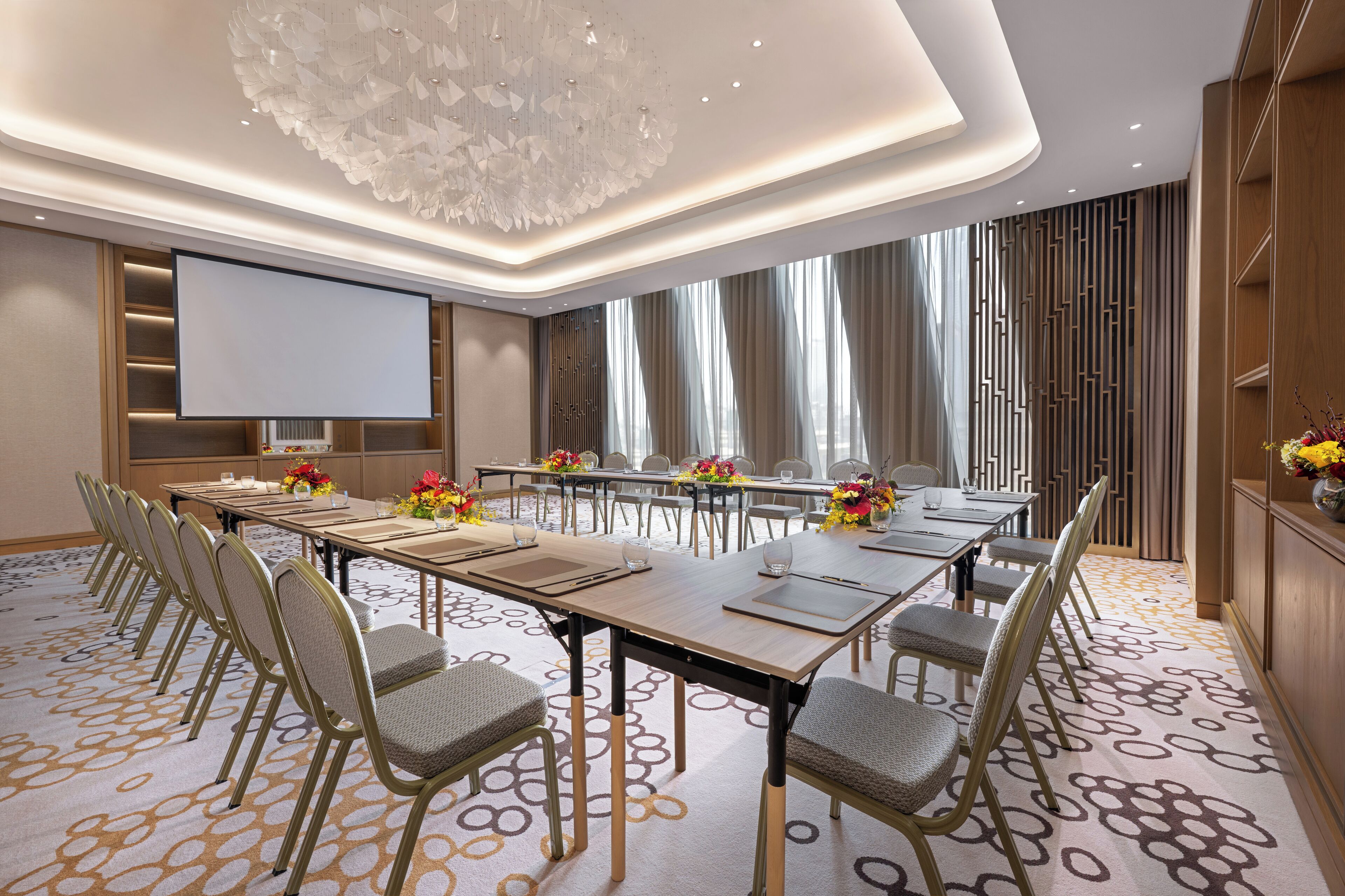 A conference room with a long table, chairs, a projector screen, and a decorative ceiling light.