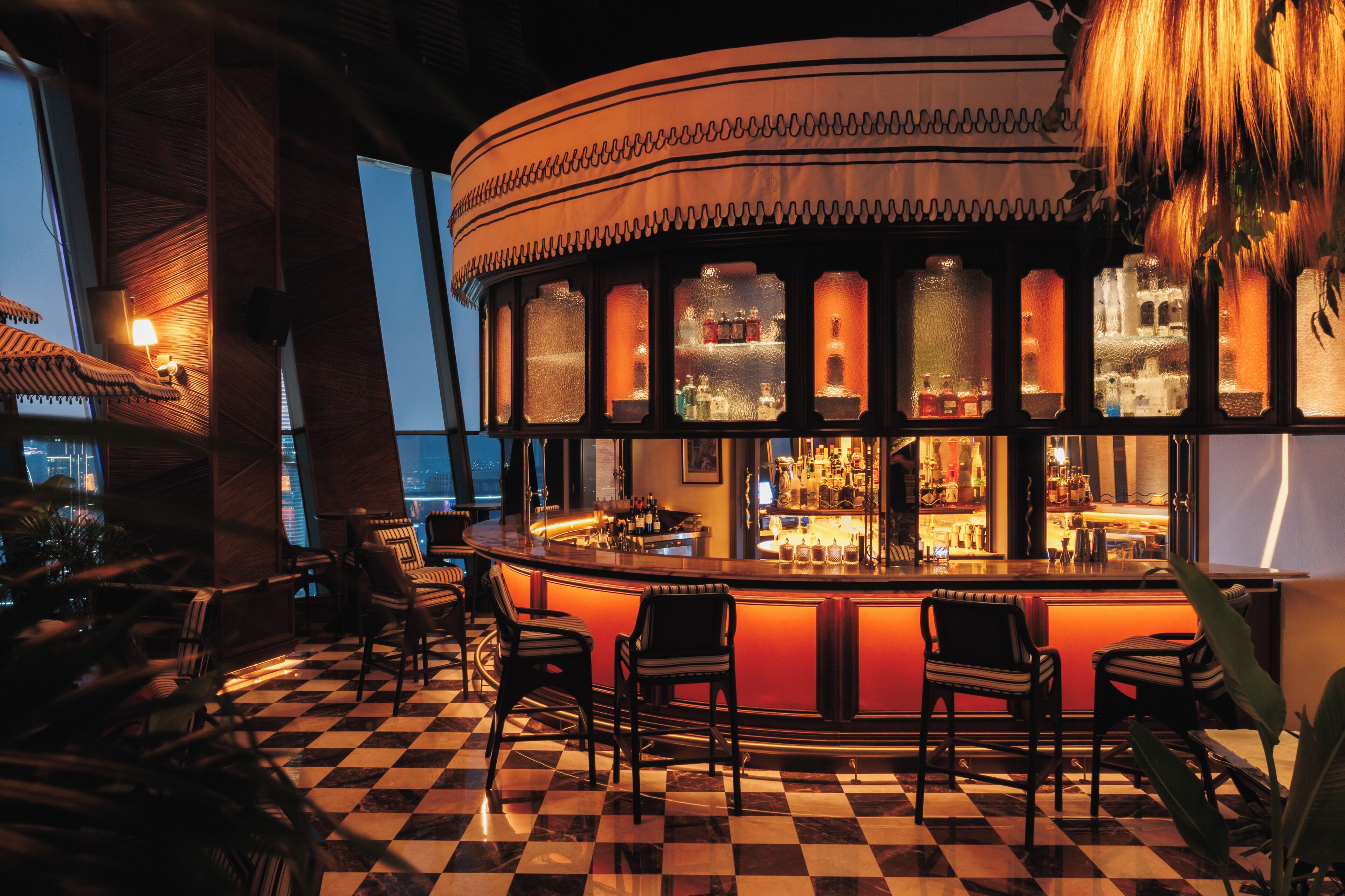 A bar with a checkered floor, bar stools, and a view of the city skyline.