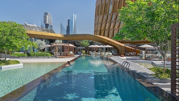 Une piscine entourée de verdure et de bâtiments modernes, avec des chaises longues et des parasols.