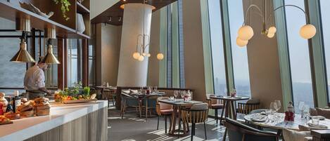 Un restaurante moderno con barra central, techos altos y grandes ventanales con vistas a la ciudad.