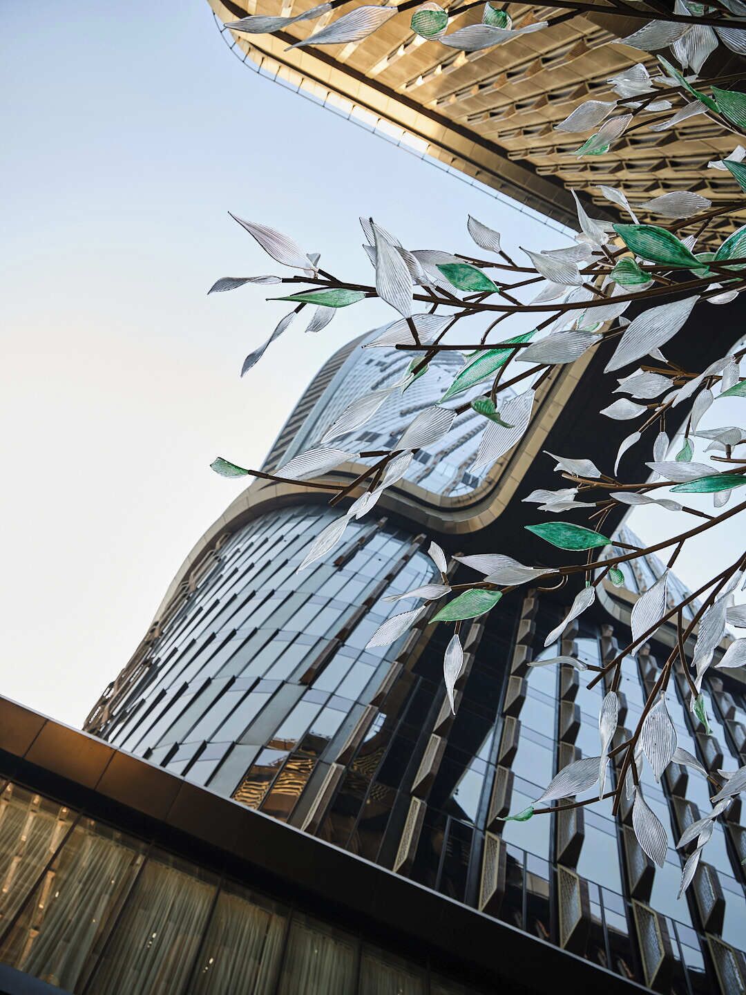 A modern building with a glass facade and a unique sculpture of leaves and branches.