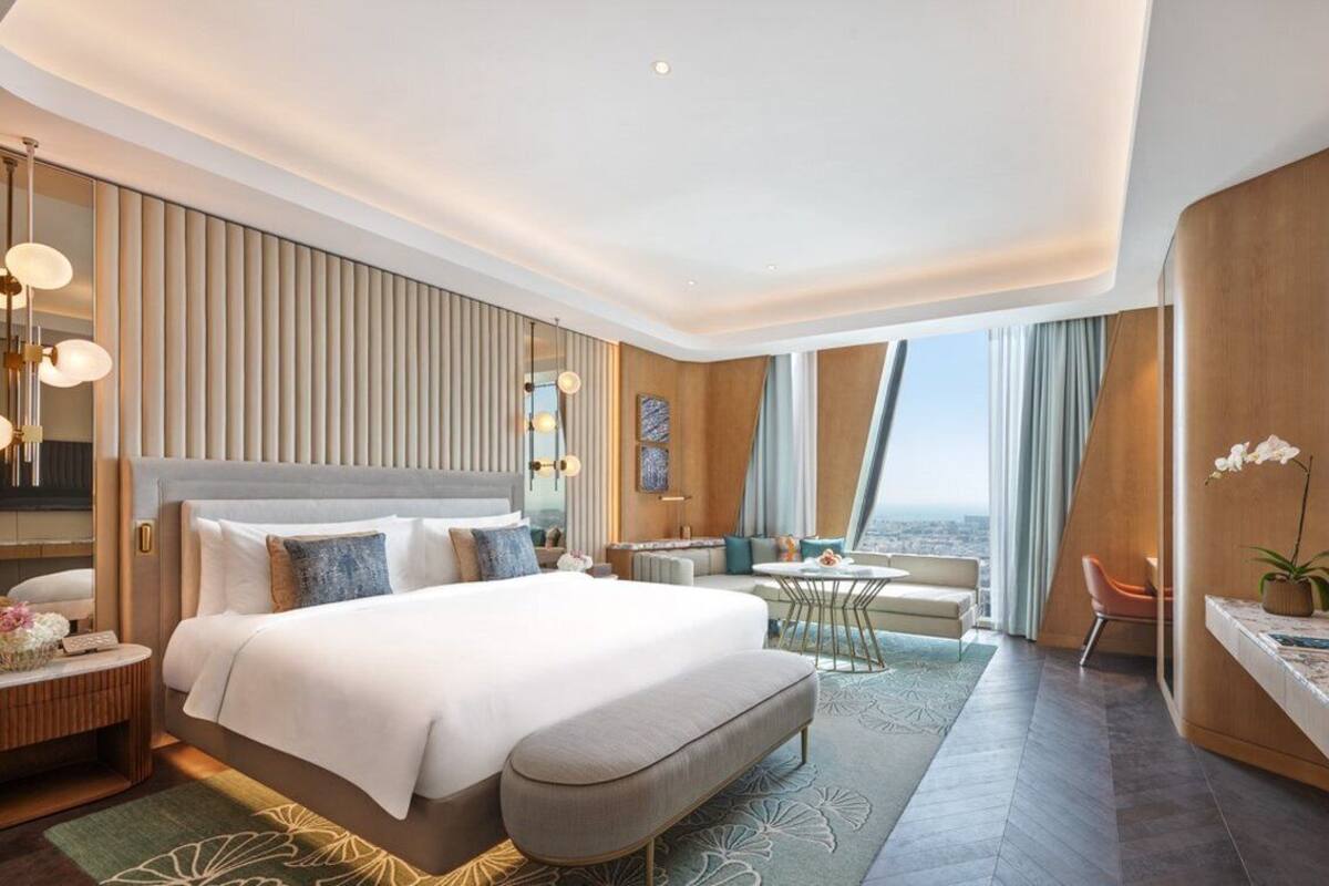 Une chambre d’hôtel moderne dotée d’un grand lit, de tables de chevet, d’un coin salon et offrant une vue sur la ville.