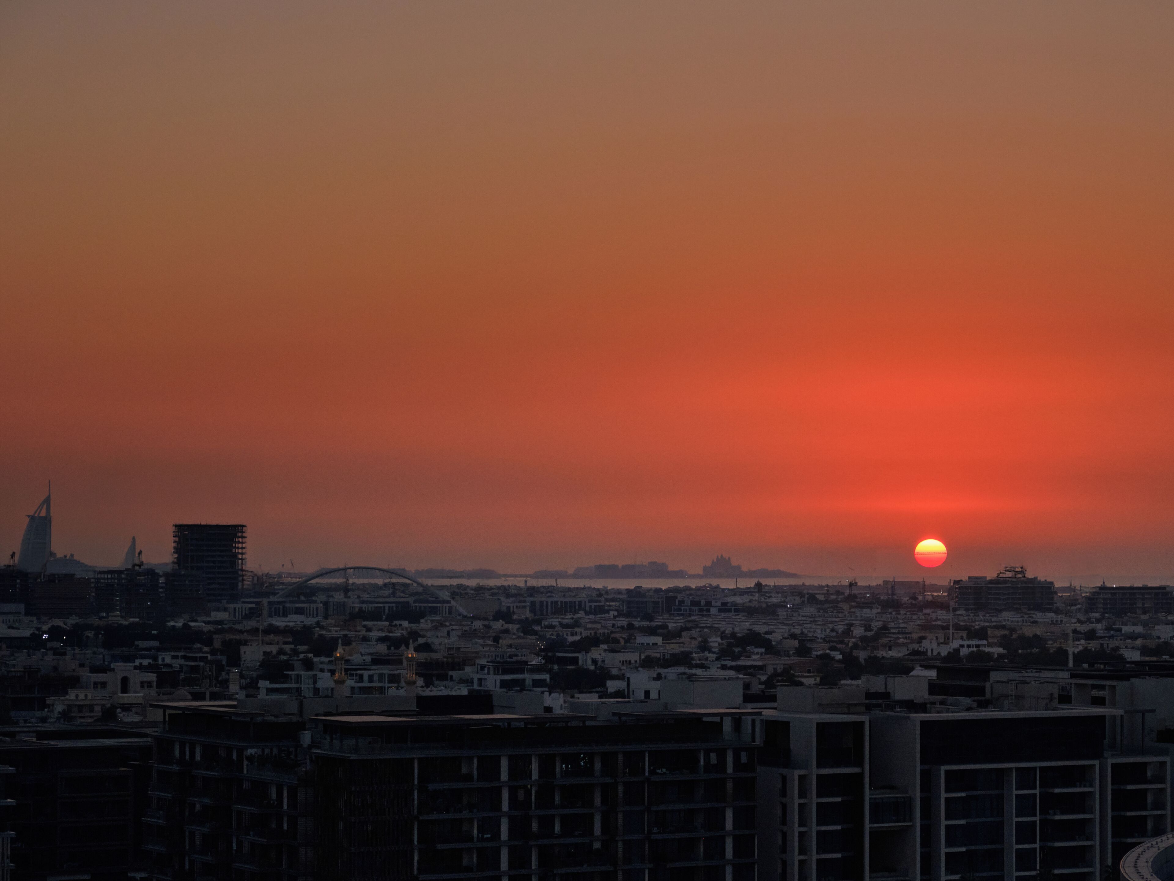 A cityscape at sunset with a prominent sun setting over buildings.