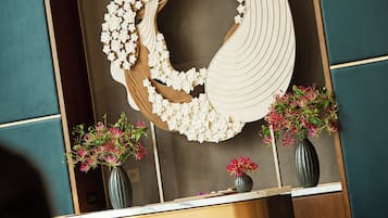 A reception desk with a modern design, a large decorative wall piece, and two vases with flowers.