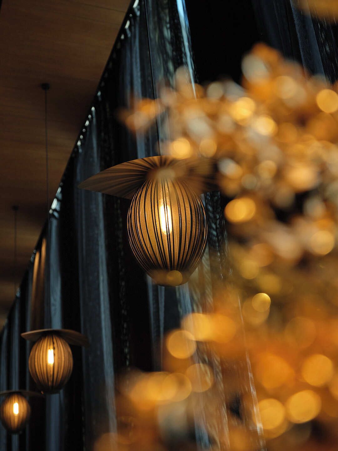 A series of hanging pendant lights with a ribbed design, suspended from a ceiling with a wooden finish.
