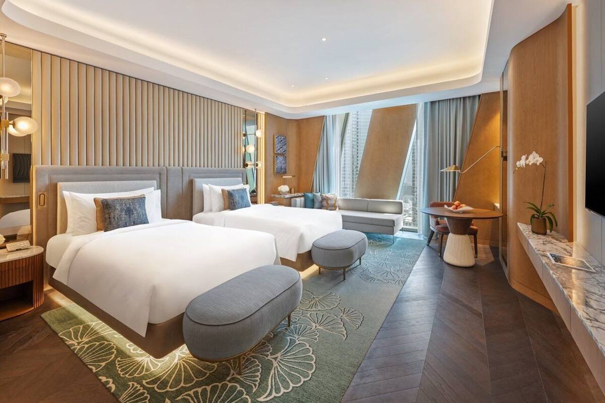 Une chambre d’hôtel moderne avec deux lits, un coin salon, une télévision et une grande fenêtre.