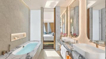 A modern bathroom with a marble bathtub, a large vanity with a mirror, and a walk-in shower.