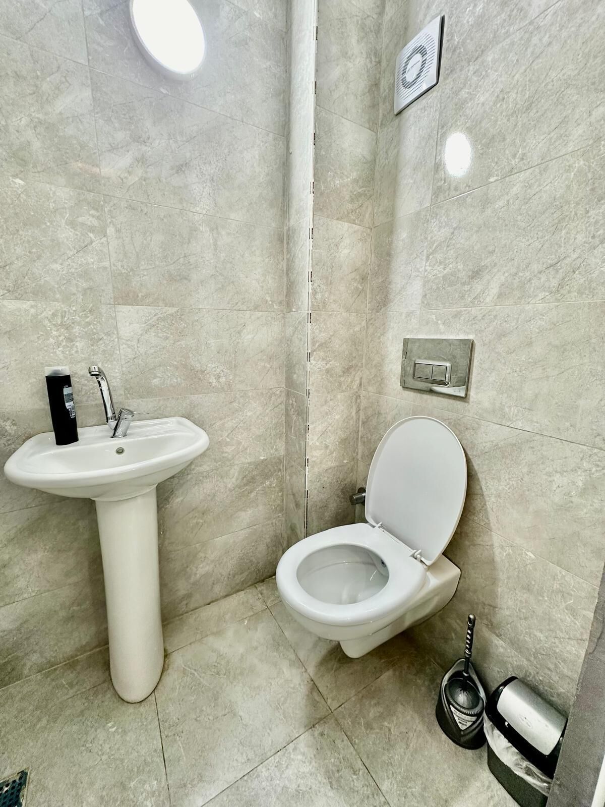 A modern bathroom with a pedestal sink, toilet, and a hand dryer.