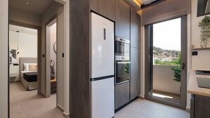 A modern kitchen with a built-in oven and refrigerator, a dining area with a table and chairs, and a view of a hillside through a large sliding glass door.