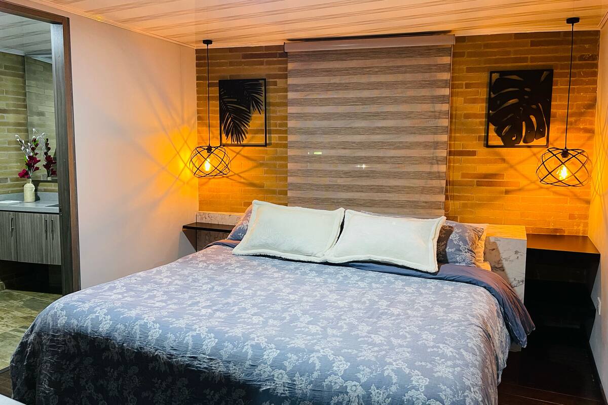 A modern bedroom with a large bed, two wall-mounted lamps, and a brick wall.