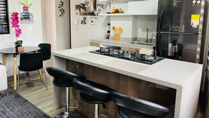 A modern kitchen with a central island, bar stools, a stainless steel refrigerator, and a gas stove. - SUITES H&A 911 (Bogotá)