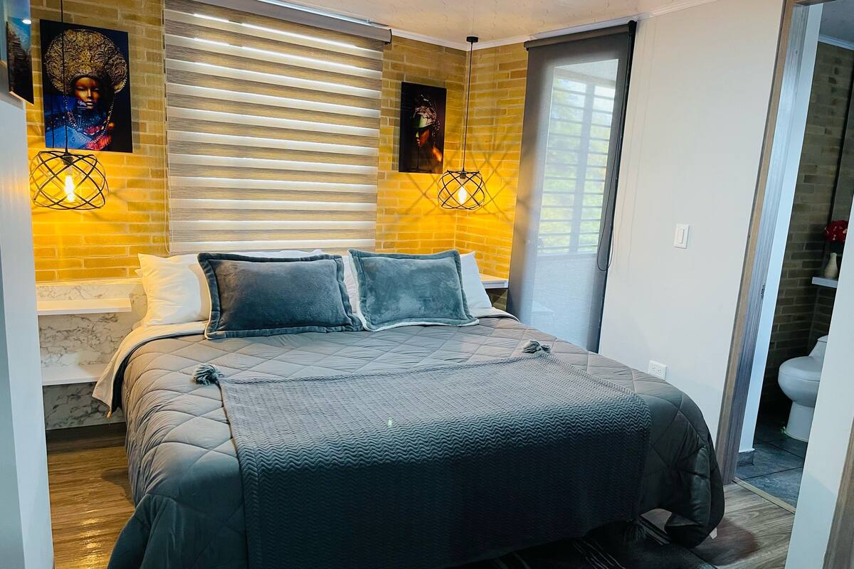 A modern bedroom with a large bed, a brick accent wall, and two wall-mounted lights.
