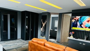 A modern lobby with a leather sofa, a mounted TV displaying a news broadcast, and a deer head decoration. - SUITES H&A 911 (Bogotá)