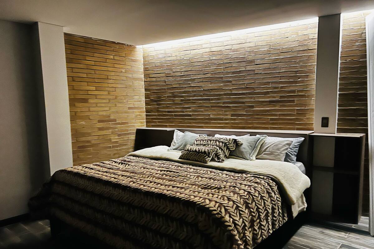 A modern bedroom with a brick-patterned headboard, a neatly made bed with patterned bedding, and a built-in bench at the foot of the bed.