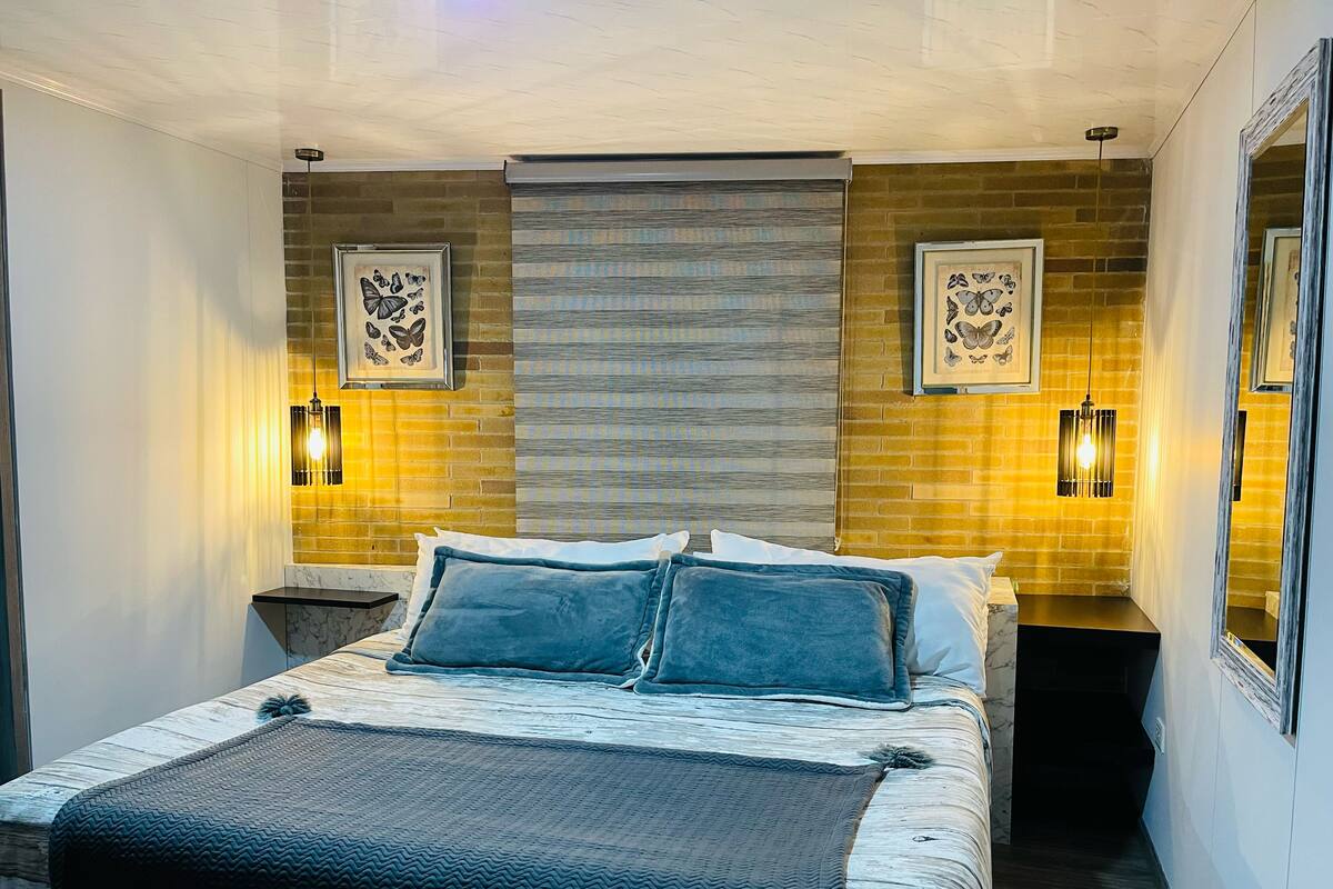 A modern bedroom with a large bed, two wall-mounted lights, and a brick wall.