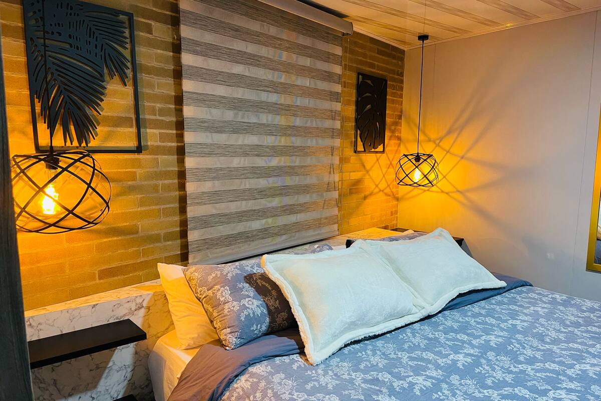 A neatly made bed with a floral bedspread, a brick-patterned headboard, and two wall-mounted light fixtures.