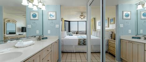 A hotel bathroom with two sinks, a large mirror, and a bed with a view of the city.