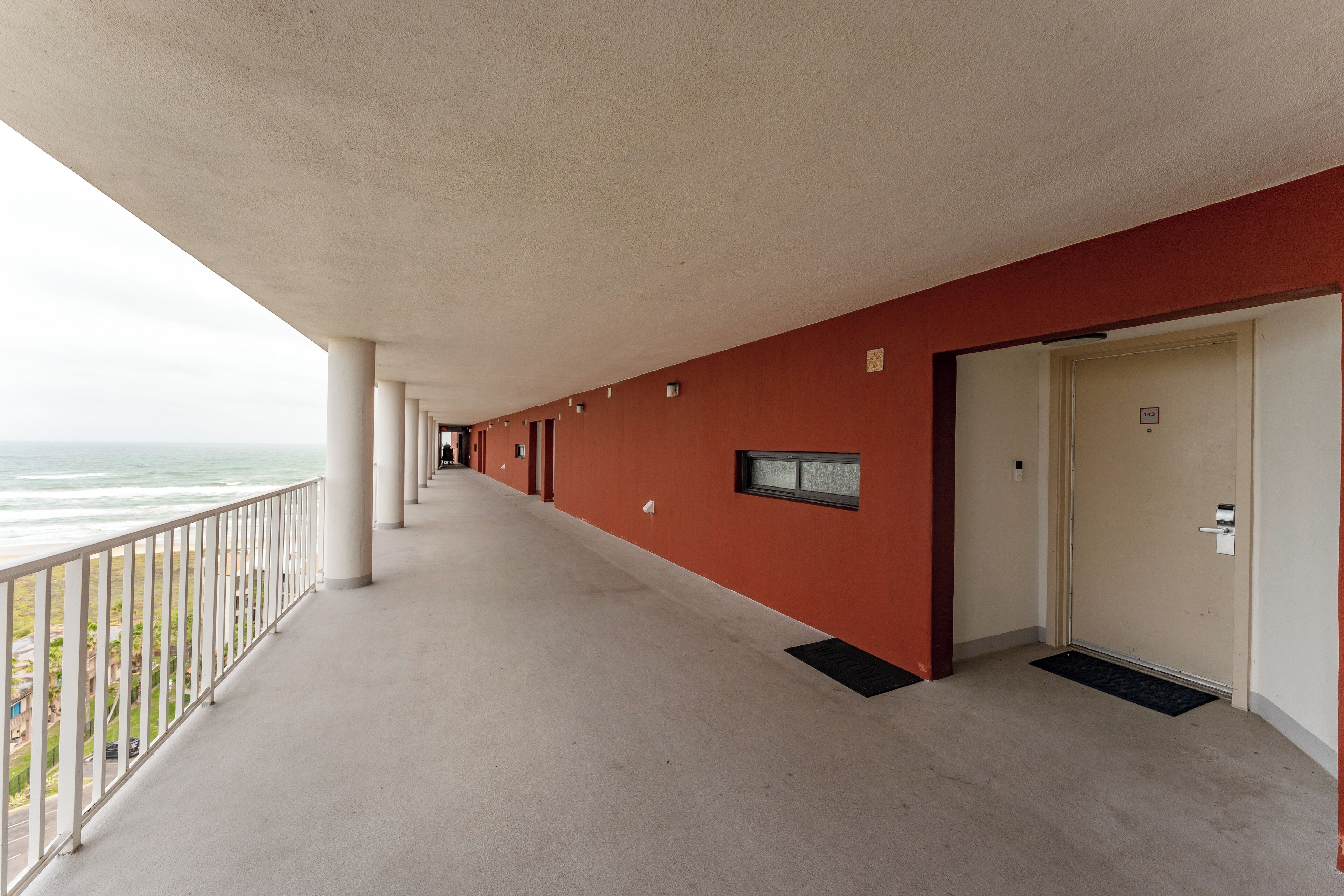 Un lungo corridoio con un balcone vista mare, caratterizzato da una parete rossa e una porta in fondo.