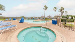 A swimming pool with lounge chairs and umbrellas, surrounded by palm trees and a brick walkway.