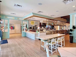 Un café moderne doté d’un bar central, de différents espaces pour s’asseoir et d’un tableau des menus bien visible.