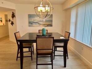 A dining area with a dark wooden table, six chairs, a chandelier, and a painting on the wall. - Towers 8 & 9 8301 - Daytona Beach Oceanfront Vacations, Inc (Ponce Inlet)