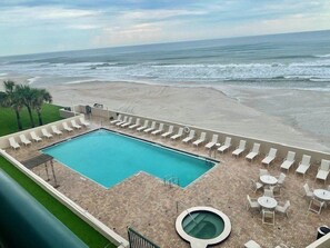 A pool area with a rectangular pool, lounge chairs, and a hot tub.