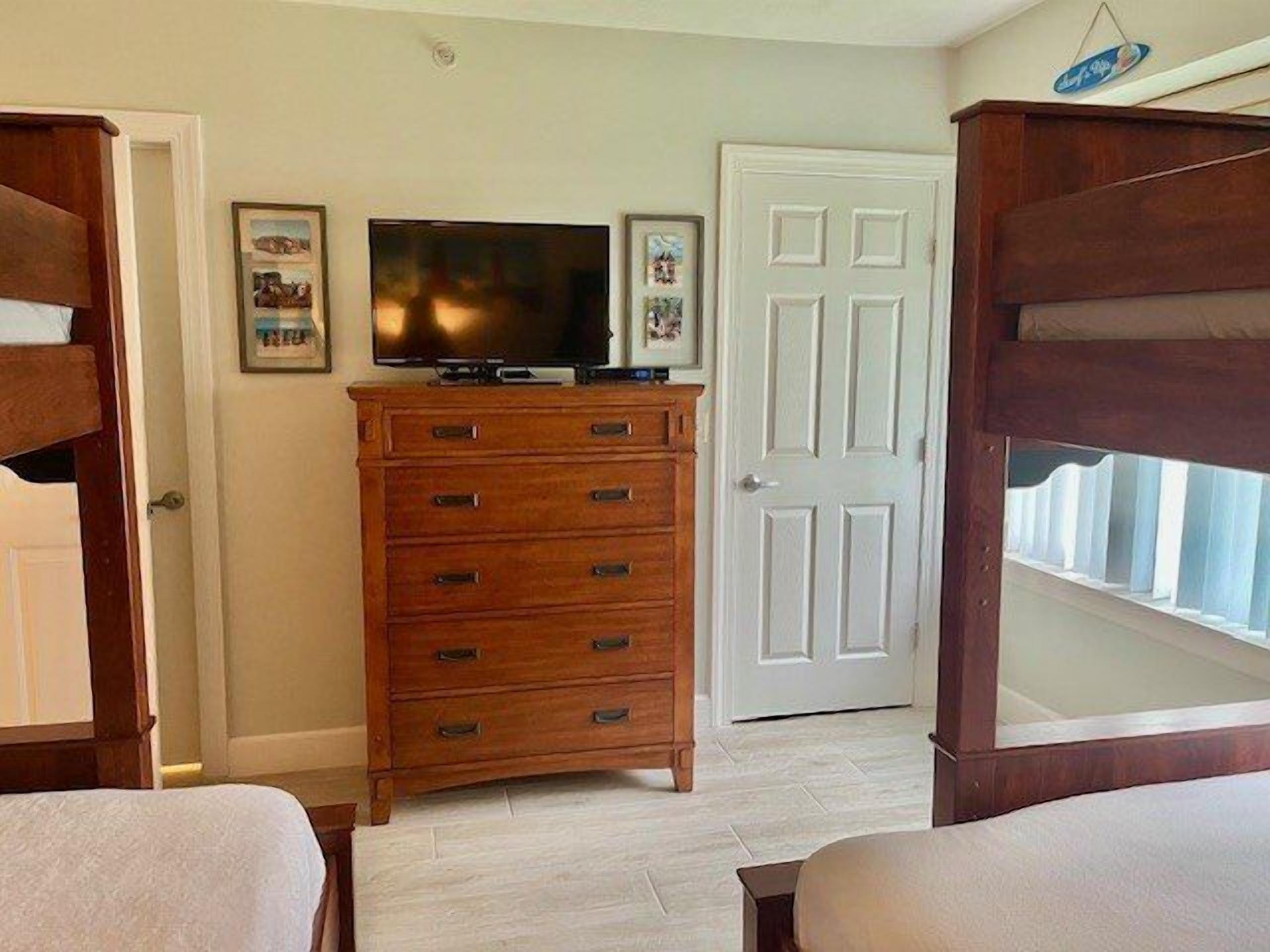 A bedroom with a wooden dresser, a television, and a white door.