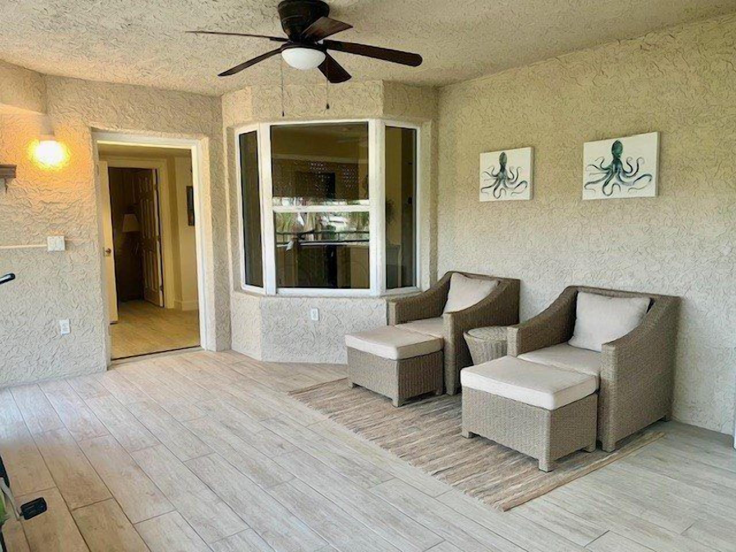 A spacious living room with a high ceiling fan, a large window, and two armchairs.
