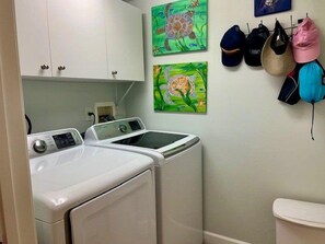 A laundry area with two front-loading washers and dryers, a white toilet, and two paintings of turtles on the wall. - Luxury at its Finest in this 3/3 Oceanfront #8301 at the Towers in Ponce Inlet (Ponce Inlet)