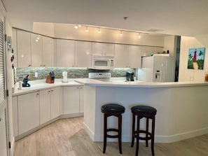 A modern kitchen with white cabinetry, a central island with stools, a microwave, and a refrigerator.