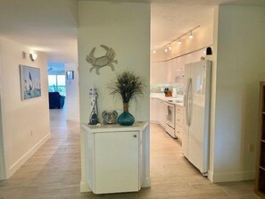 A modern kitchen with white cabinets, a built-in oven, and a refrigerator. There is a small white cabinet with decorative items on top. - Luxury at its Finest in this 3/3 Oceanfront #8301 at the Towers in Ponce Inlet (Ponce Inlet)