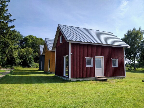 Une cabane en bois rouge, avec un toit en métal, une porte et deux fenêtres.