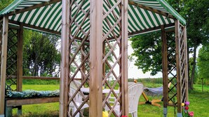 A wooden gazebo with a green and white striped roof, surrounded by grass and trees. - Urlaub in Masuren - Ferienhaus, Angelurlaub (Iława)