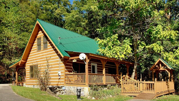 Una cabaña de troncos con techo verde, un porche y una pequeña terraza.