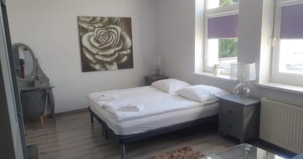 A bedroom with a bed, bedside tables, a mirror, a window with blinds, and a radiator. - Pensjonat U Aktorów (Elblag)