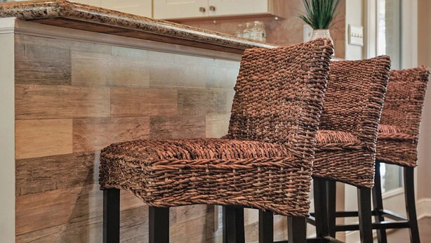 Eine Küche mit einer Holz-Fischgrätverkleidung, weißen Schränken und drei Korbstühlen.