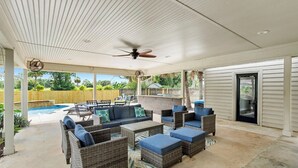 Eine überdachte Terrasse mit Korbmöbeln, einem Deckenventilator und einem Pool im Hintergrund.