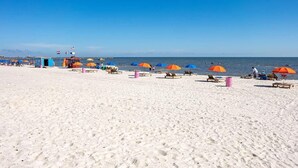 A beach with rows of sun loungers and umbrellas, a lifeguard station, and the ocean in the background. - Private Pool w/Heating Option! 5Bedrooms & Close to Biloxi! (Gulfport)
