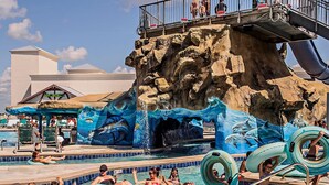 A pool area with a rocky backdrop, inflatable rings, and a water slide. - Private Pool w/Heating Option! 5Bedrooms & Close to Biloxi! (Gulfport)