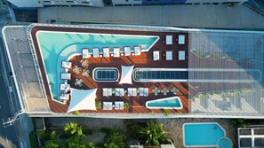 An aerial view of a cruise ship deck with a swimming pool, sun loungers, and a covered seating area.