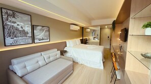 A modern hotel room with a large bed, a sofa, a TV, and artwork on the wall.
