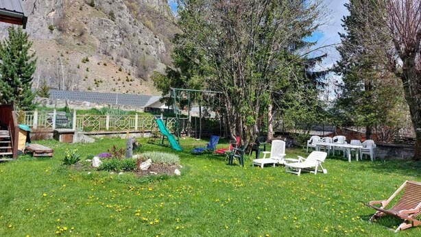 Een gazon met een speeltuin, witte lounge stoelen en een berg op de achtergrond.