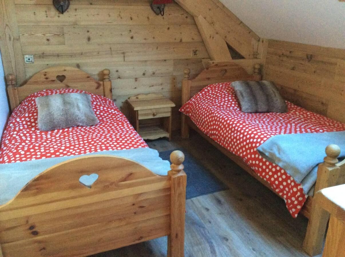 A cozy attic bedroom with two wooden beds, each with a heart-shaped headboard, and a small wooden nightstand between them.