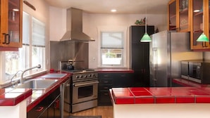 A modern kitchen with stainless steel appliances, wooden cabinets, and a red-tiled island.