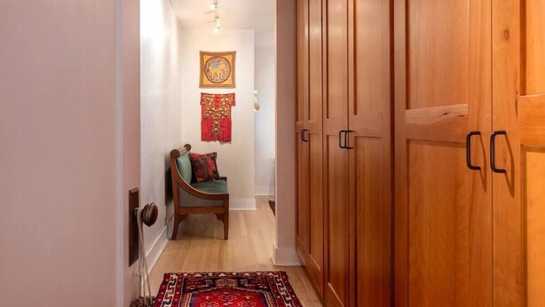 A hallway with wooden cabinets, a chair, a patterned rug, and a wall-mounted picture.