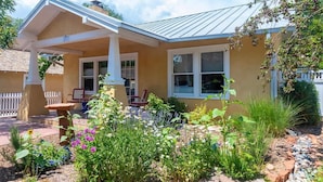 A house with a covered porch, a garden with various plants and flowers, and a brick pathway.