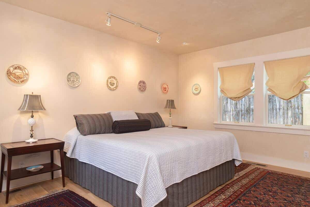 A bedroom with a bed, bedside tables, decorative plates, and a window with curtains.