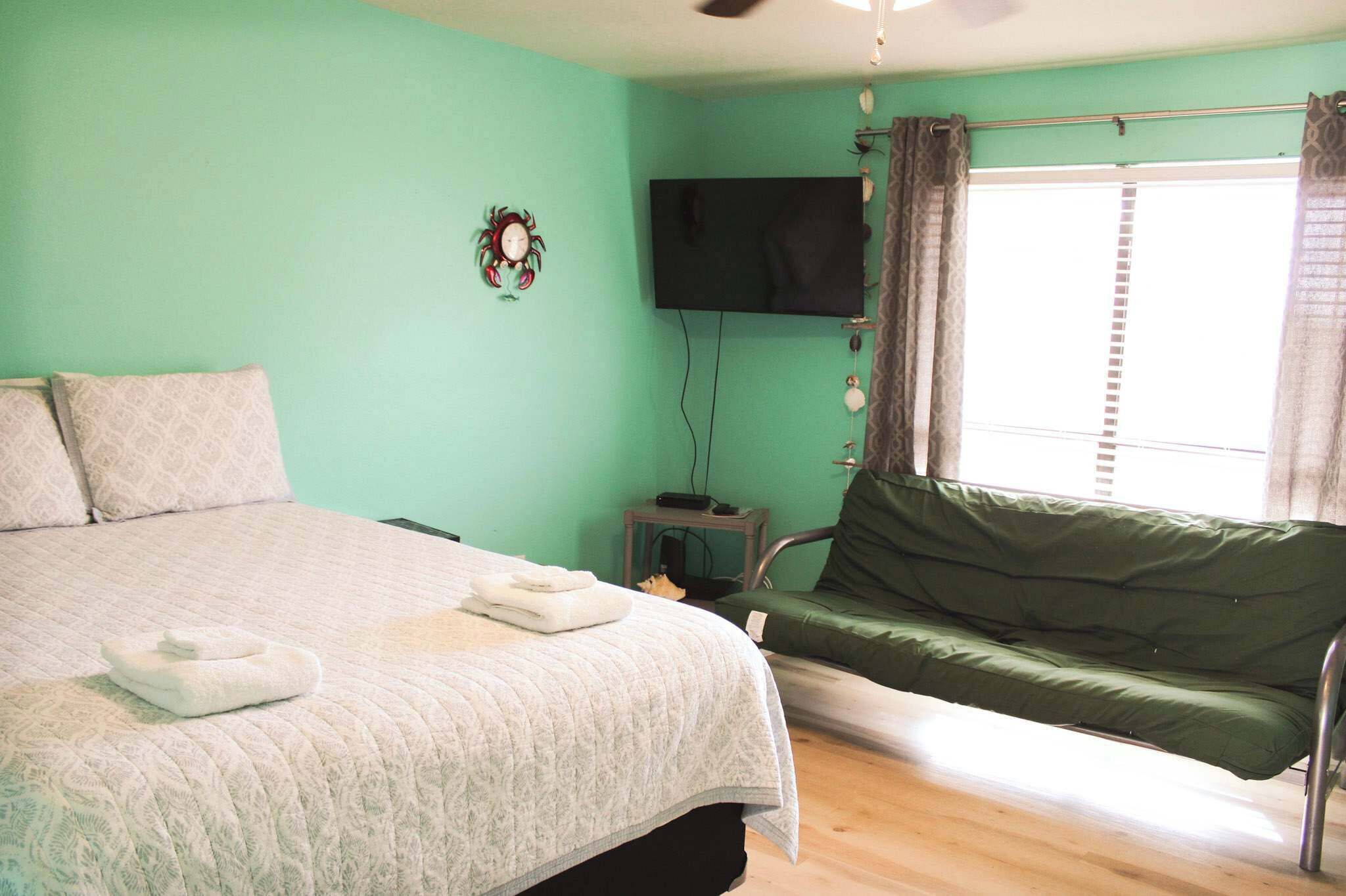 A room with a bed, a green sofa, a television, and a window with curtains.