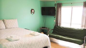 Ein Zimmer mit einem Bett, einem grünen Sofa, einem Fernseher und einem Fenster mit Vorhängen.