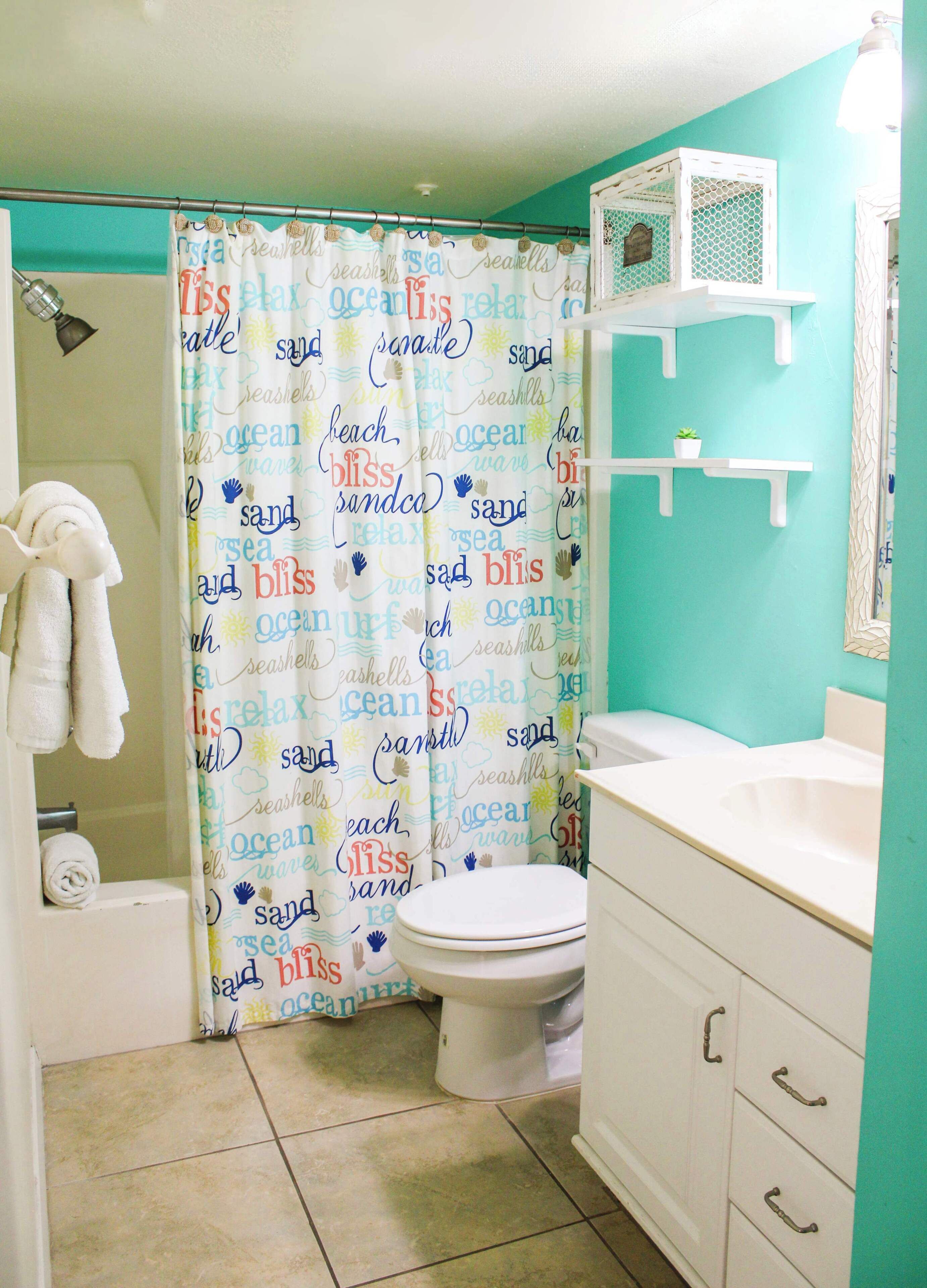 Un baño con inodoro, lavamanos y cortina de ducha decorada con motivos marinos.